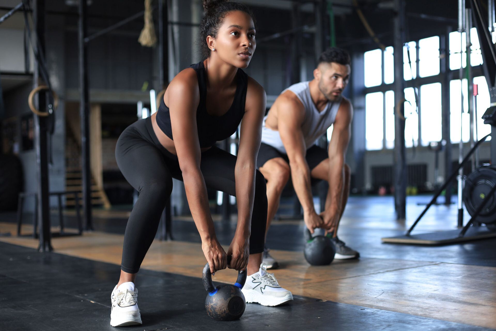 A man and a woman are lifting kettlebells in a gym