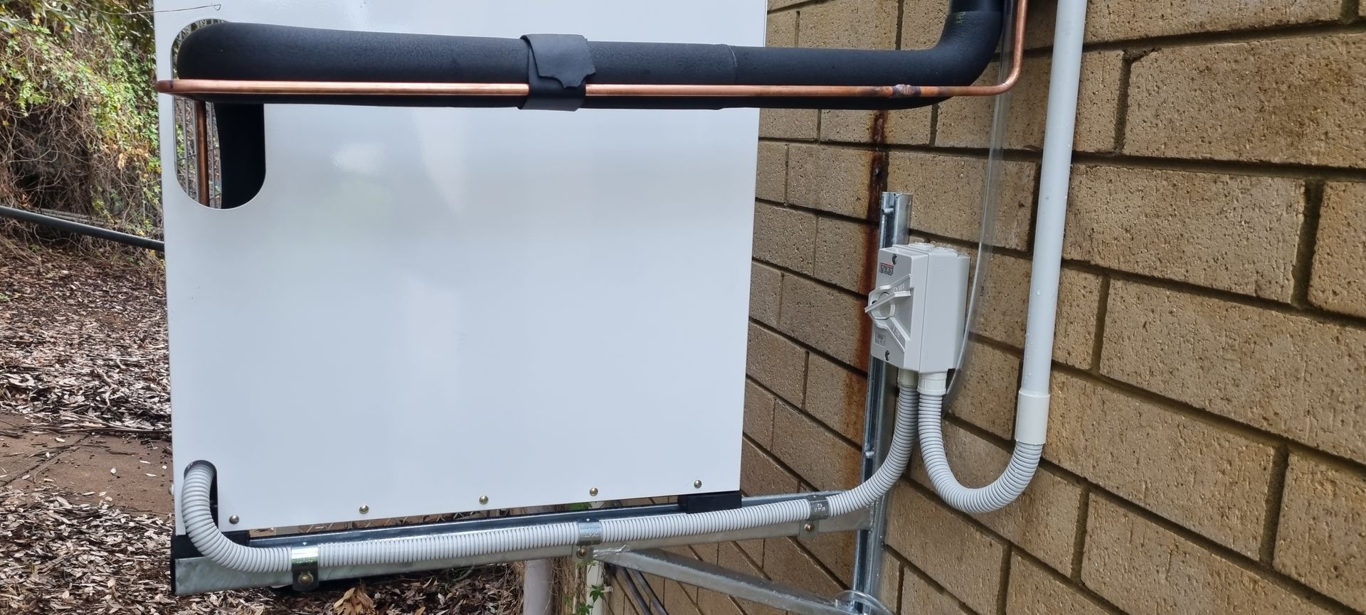 A brick wall with a white box and pipes attached to it.