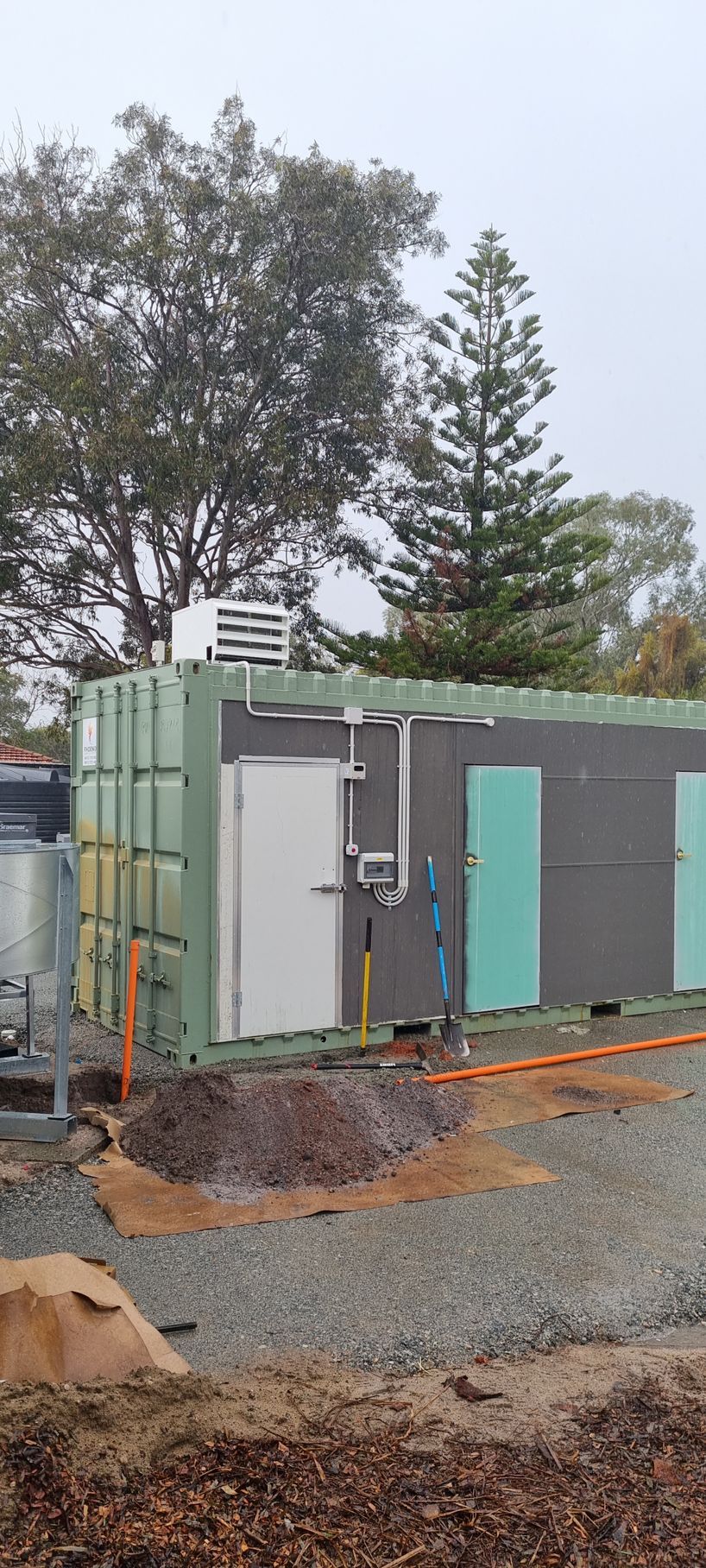 A large green building with blue doors is sitting on top of a dirt field.
