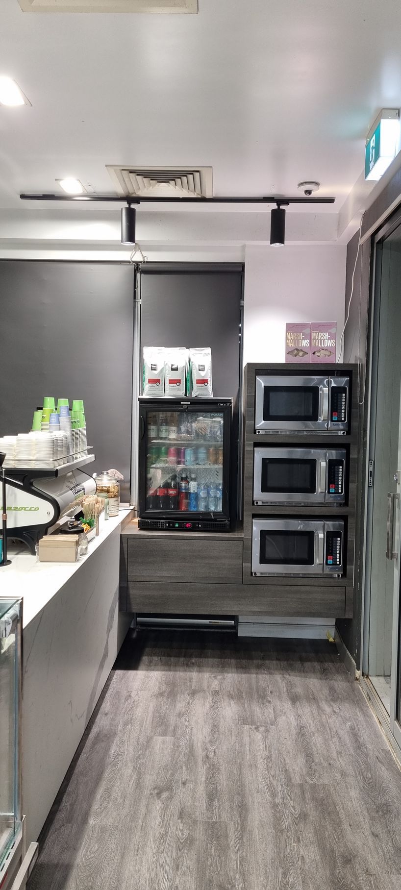 A long hallway in a restaurant with three microwaves and a refrigerator.