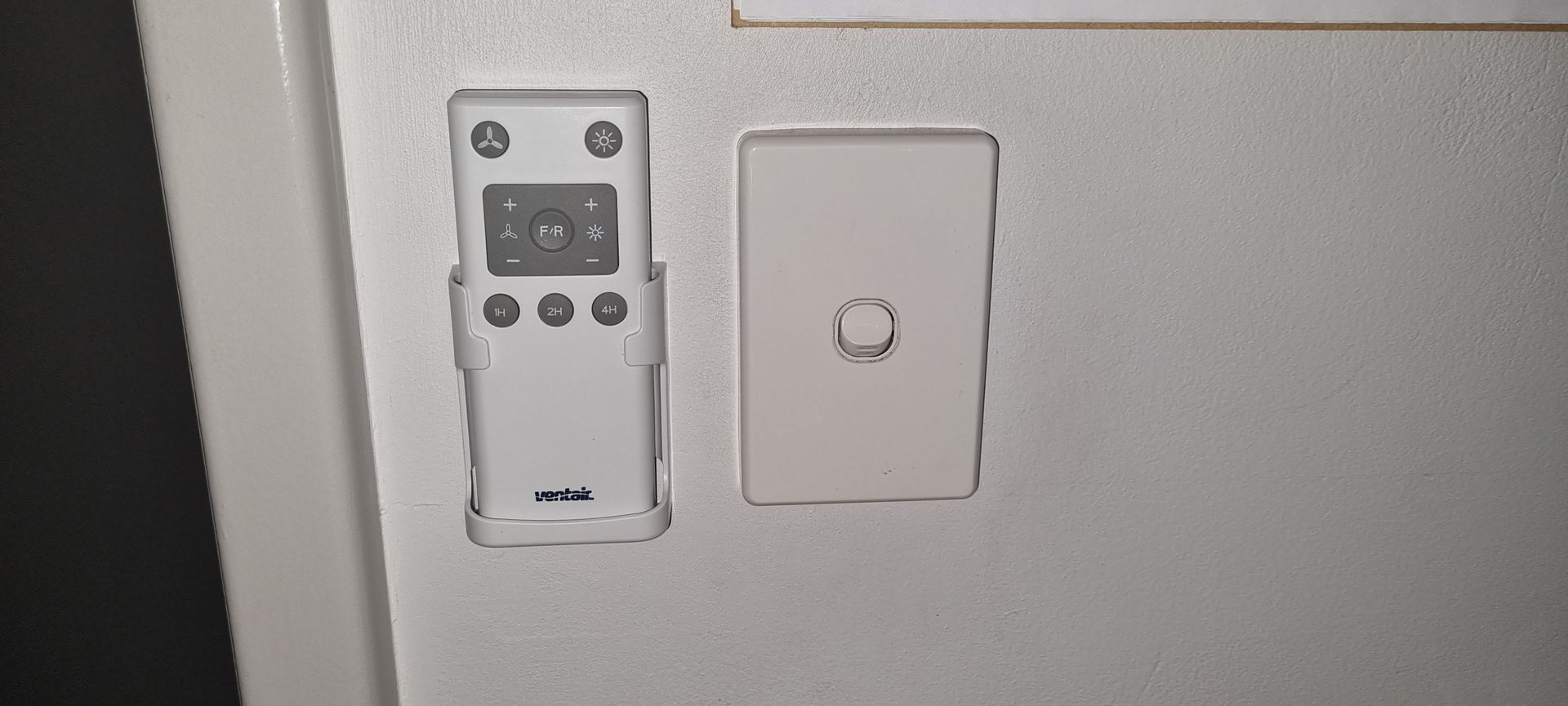 A picture of a remote control and a light switch on a wall.