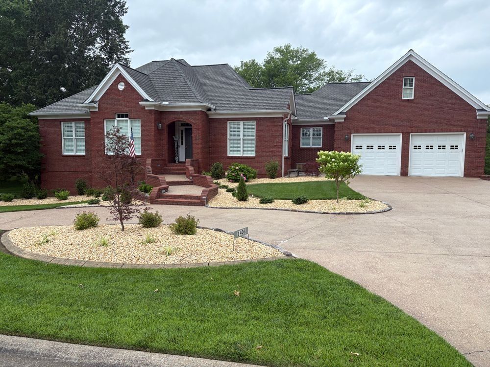 Red brick house with white garage doors, tan driveway, and landscaped yard.
