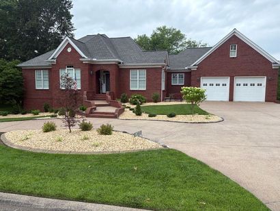 Red brick house with white garage doors, tan driveway, and landscaped yard.