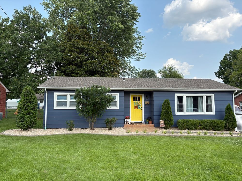 Blue house with yellow door, white trim, and well-manicured lawn and landscaping.