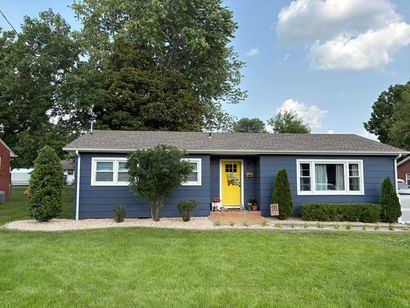 Blue house with yellow door, white trim, and well-manicured lawn and landscaping.