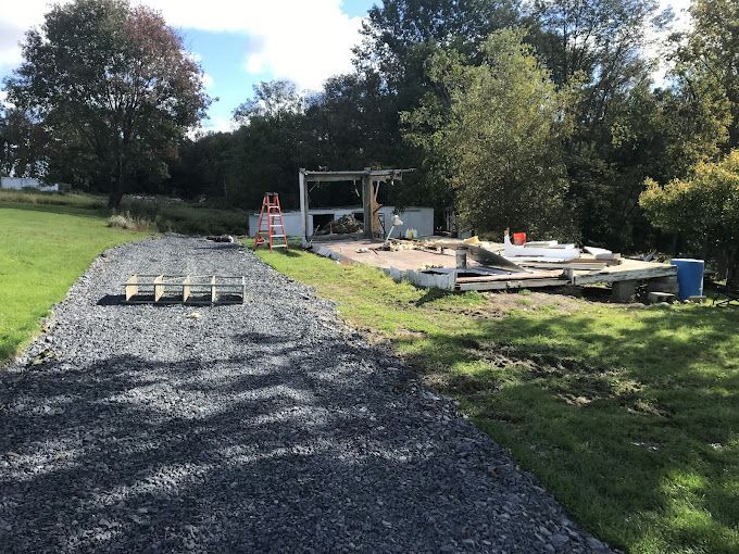 A gravel road going through a grassy field with a building in the background.