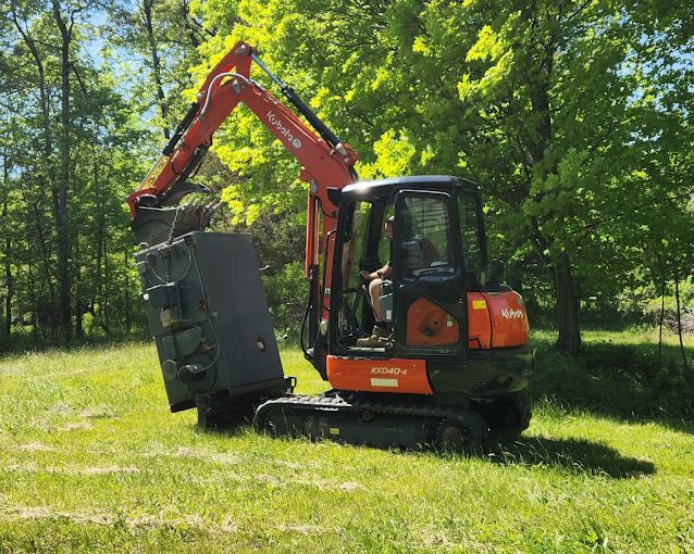 A small orange and black excavator is sitting in a grassy field.