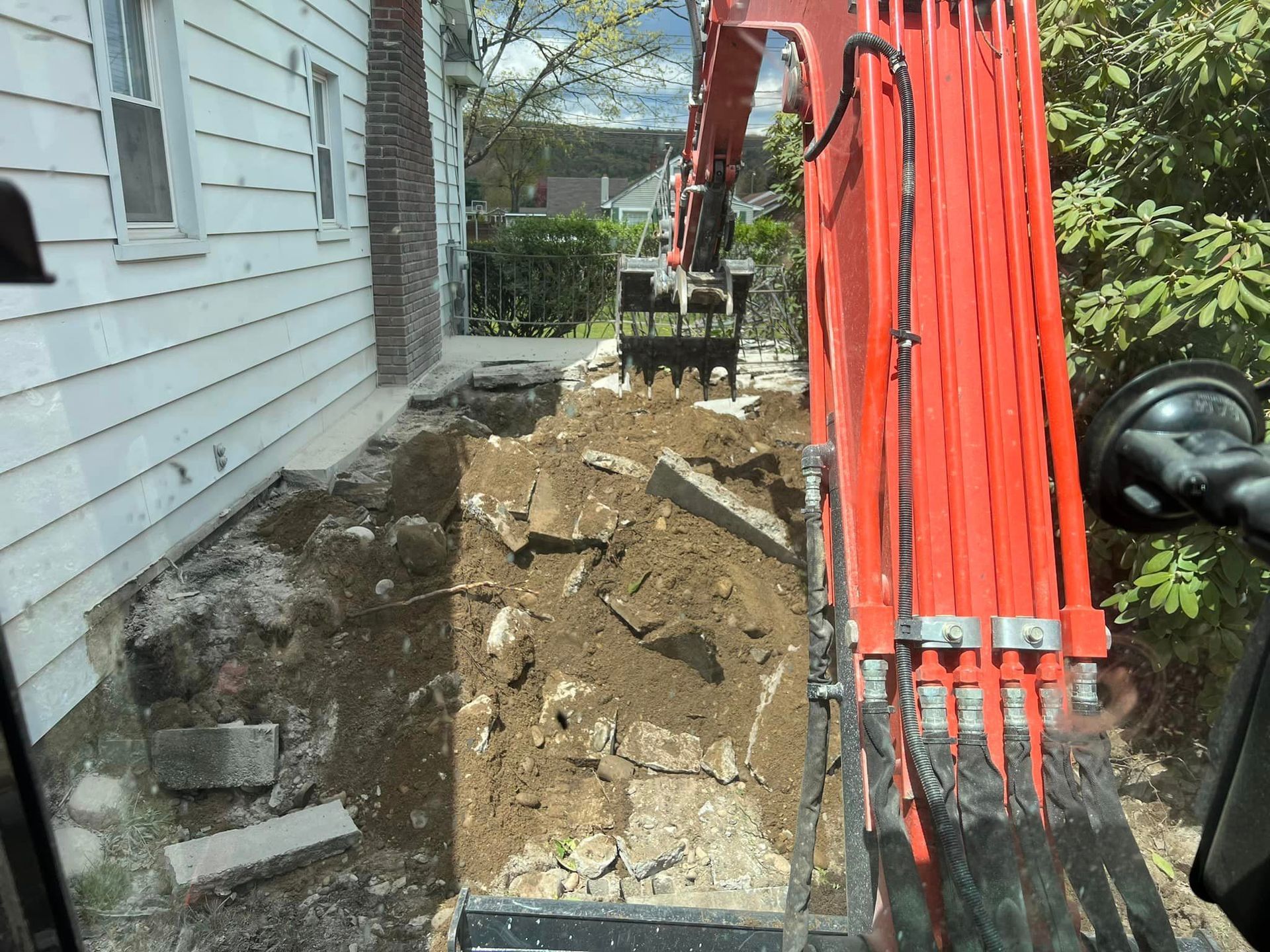 A red excavator is digging a hole in front of a house