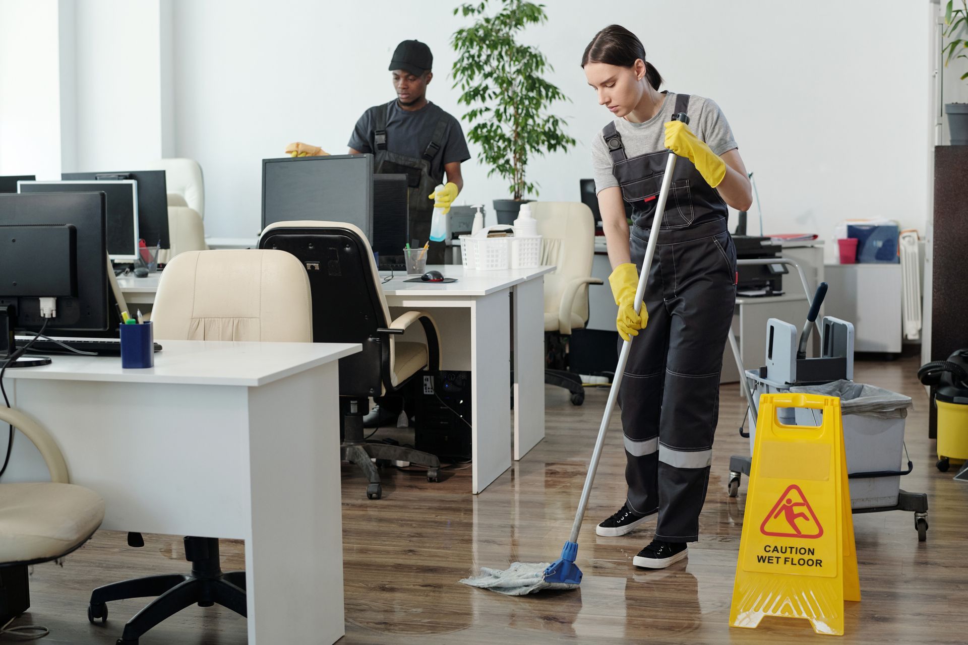 A woman is cleaning the floor of an office with a mop.