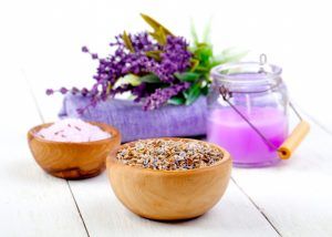 Lavender-themed spa setup: lavender bouquet, purple candle, bowls of bath salts and lavender buds.