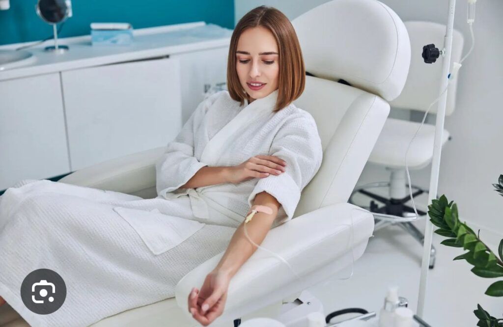 Woman in white robe receives IV drip in a modern spa-like setting.