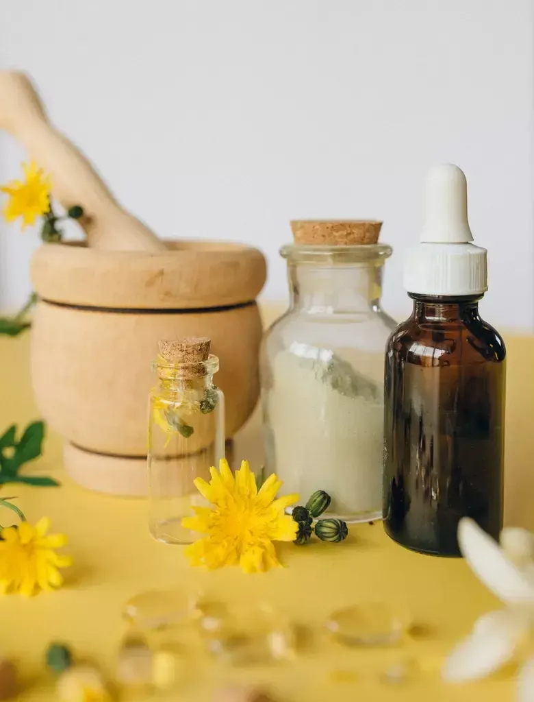 Wooden mortar and pestle, glass bottles, yellow flowers, and capsules on a yellow surface.
