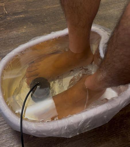 Person soaking feet in a foot bath, a black device visible in the water.