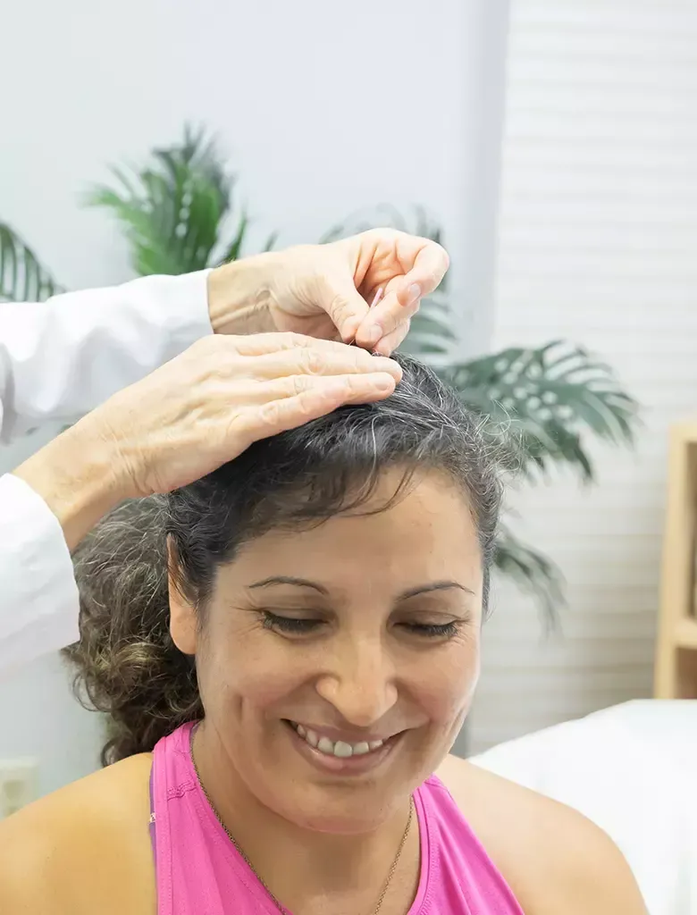 Woman receiving acupuncture on her head; doctor's hands inserting needles. She smiles in a medical setting.
