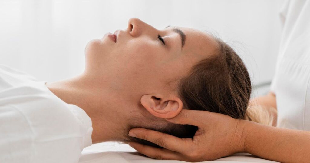 Woman receiving neck massage in a light-filled room. Someone's hands supporting her head.