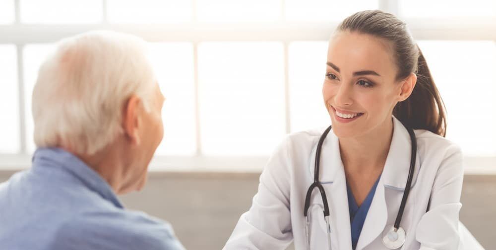 Young doctor smiles while speaking to older patient in a brightly lit office.