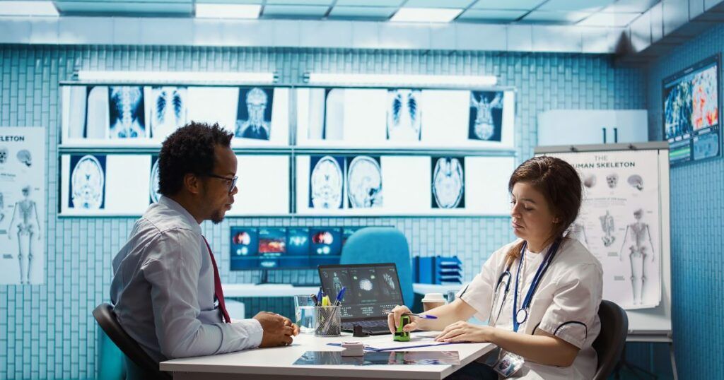 Doctor and patient at a desk; X-rays on wall. Doctor stamps a form, while patient looks on.
