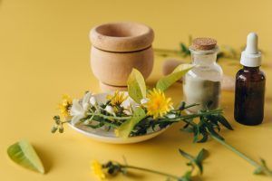 Herbal medicine setup with flowers, mortar, bottles, and a dropper on a yellow background.
