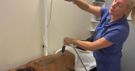 Woman administering therapy on a person's back, using a handheld device. Light-colored room.