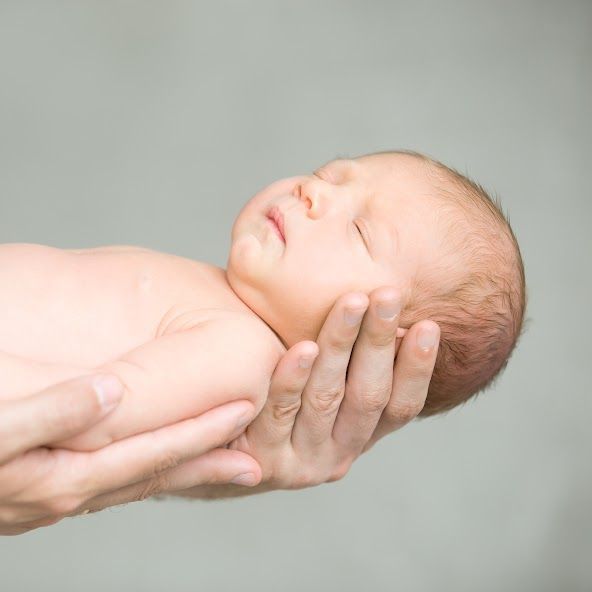 Sleeping newborn baby held gently in someone's hands.