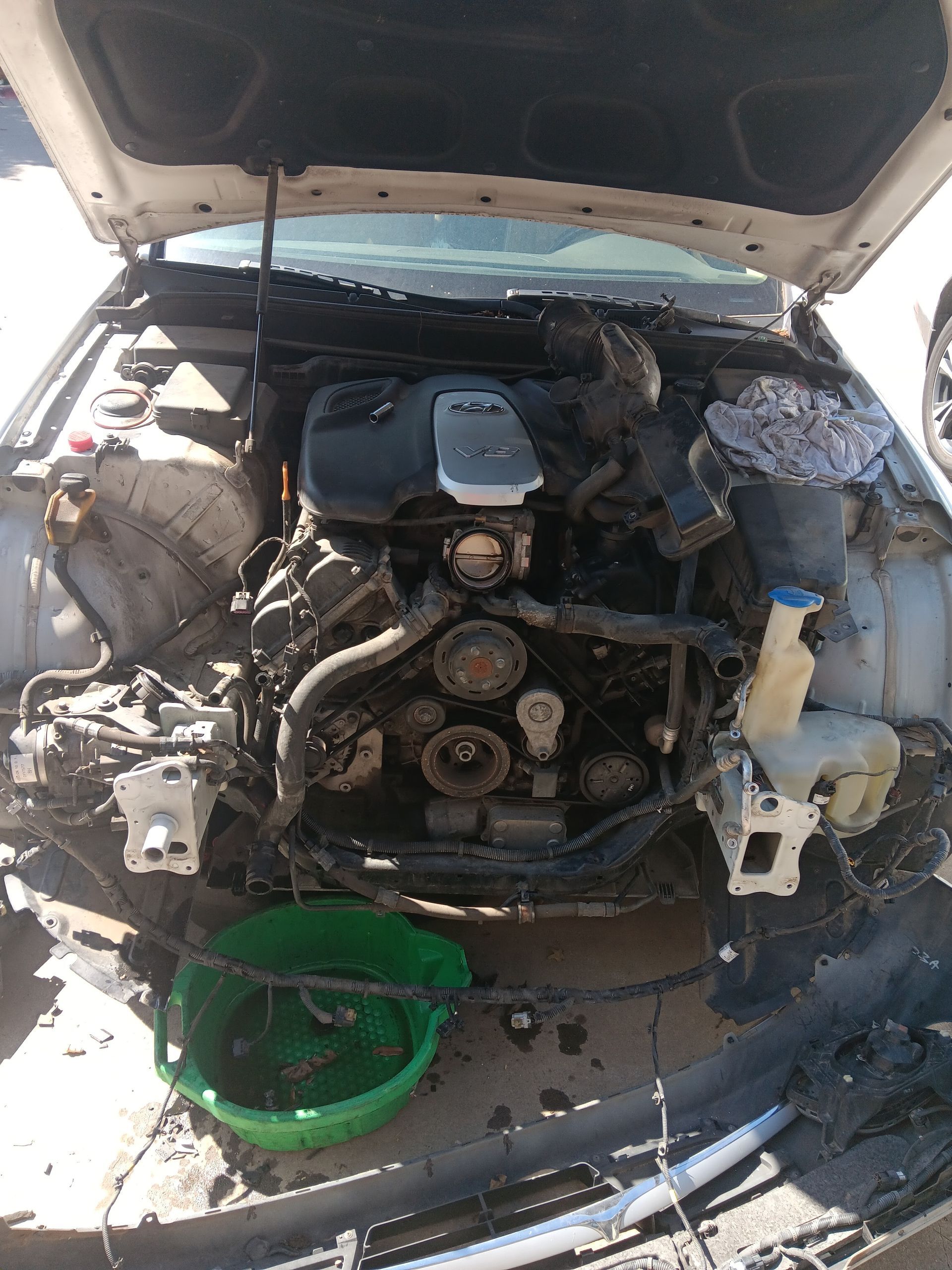 A car with the hood up and a green bucket next to it.