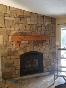 Rustic indoor stone fireplace with wood mantel after chimney restoration service.