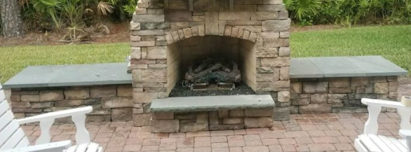 Outdoor stone fireplace installation and chimney repair in backyard patio.