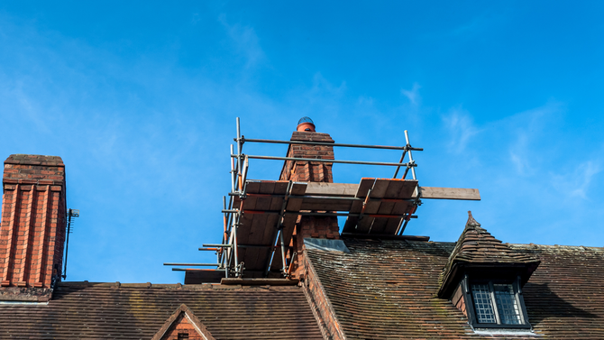 A brick chimney is being repaired on the roof of a house.