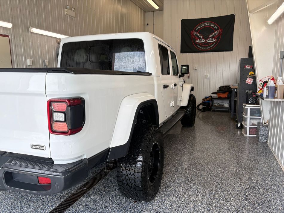 White pickup truck parked in a garage with a polished speckled floor and black wall banner