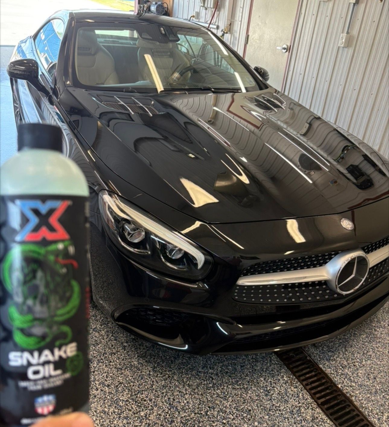 Black Mercedes-Benz in a garage, with a bottle of Snake Oil car detailer in the foreground.