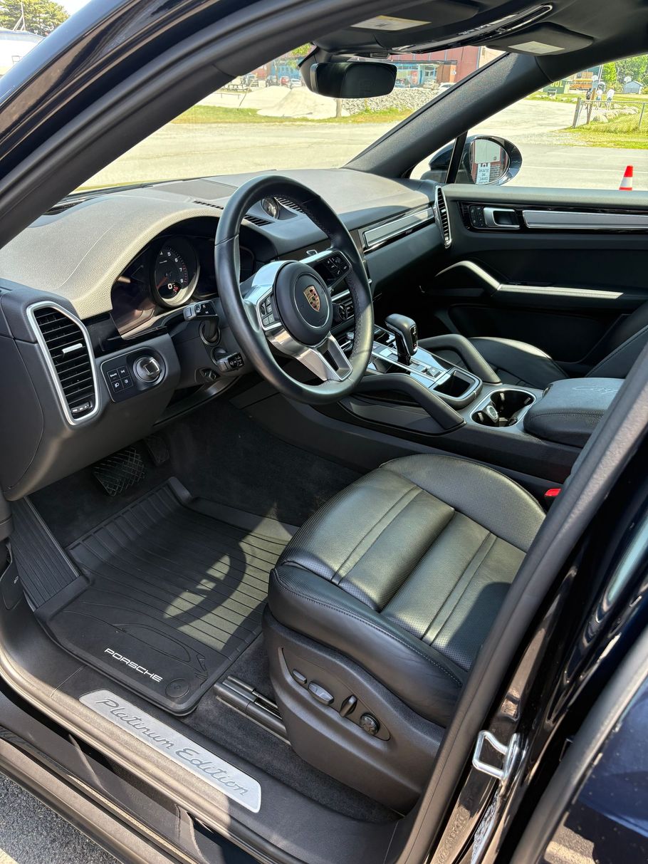 Open car door showing black leather sports car interior with steering wheel and dashboard