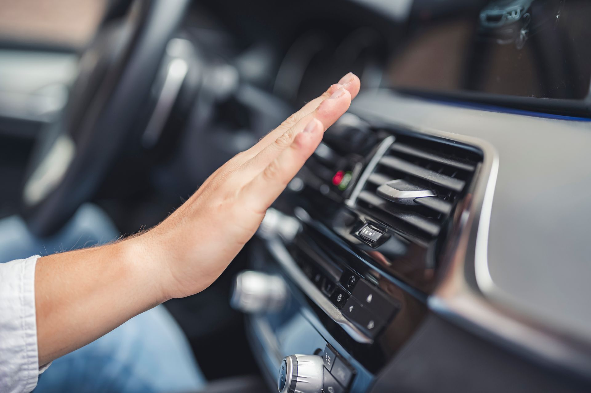 A person holds their hand up to the car's air conditioning vent, feeling the warm air coming out. 