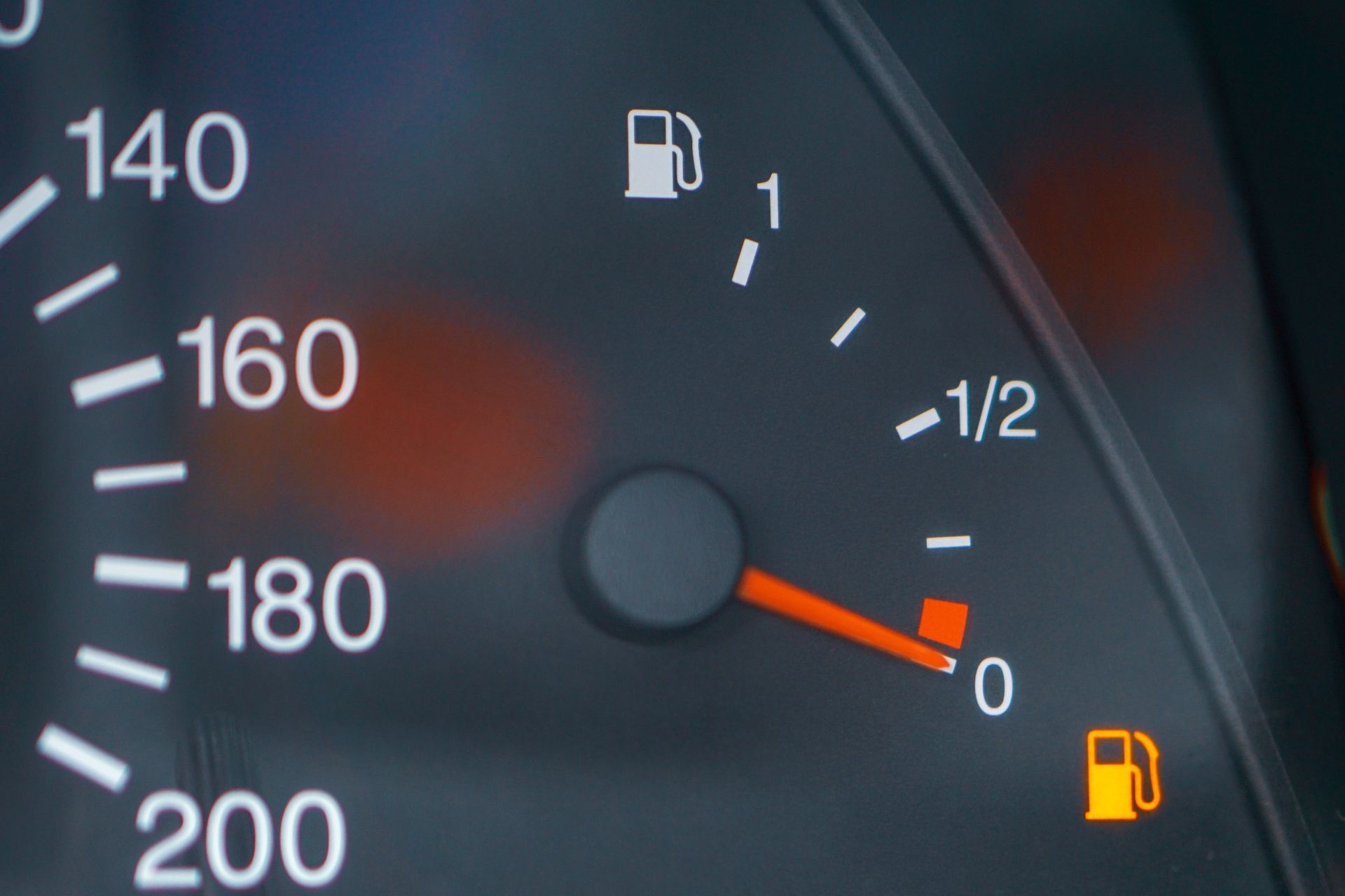 Close-up of a car dashboard with the fuel gauge indicating low fuel and the gas light illuminated.