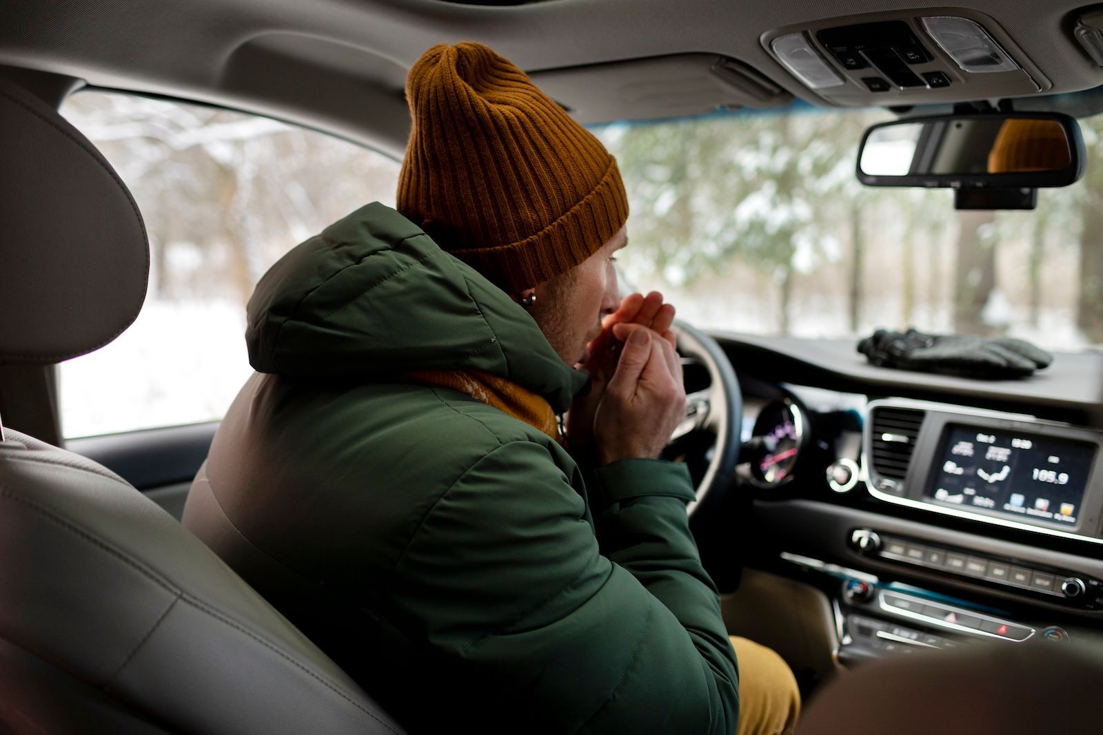 A man sitting in his car, blowing into his hands to warm them up on a cold day, with the heater not 