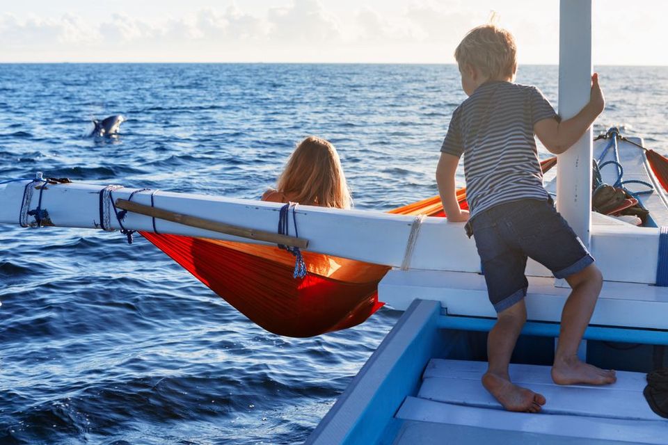 A boy and a girl are sitting in a hammock on a boat in the ocean.