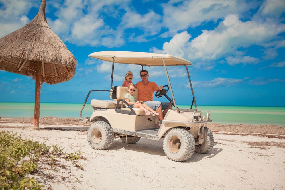 A man and two children are sitting in a golf cart on the beach.