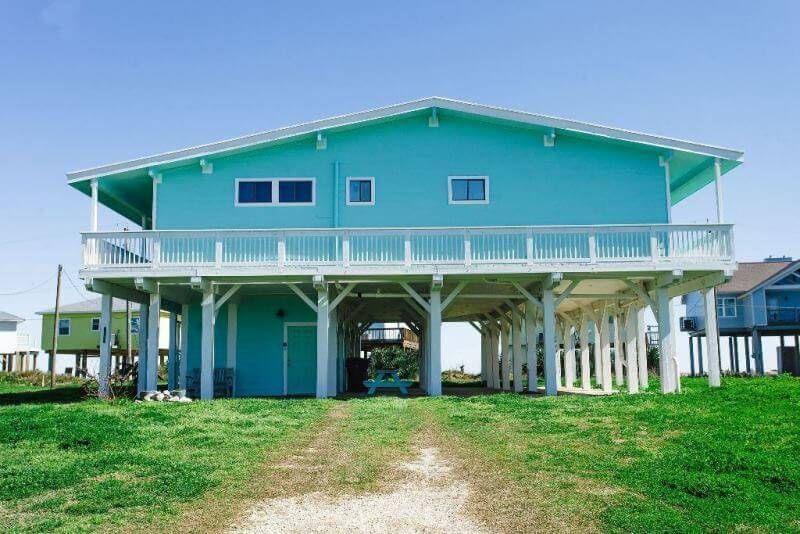 A large blue house with a large deck is sitting on top of a lush green field.