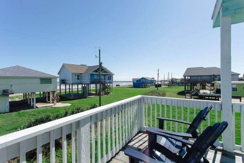 A balcony with two chairs and a view of houses and the ocean.