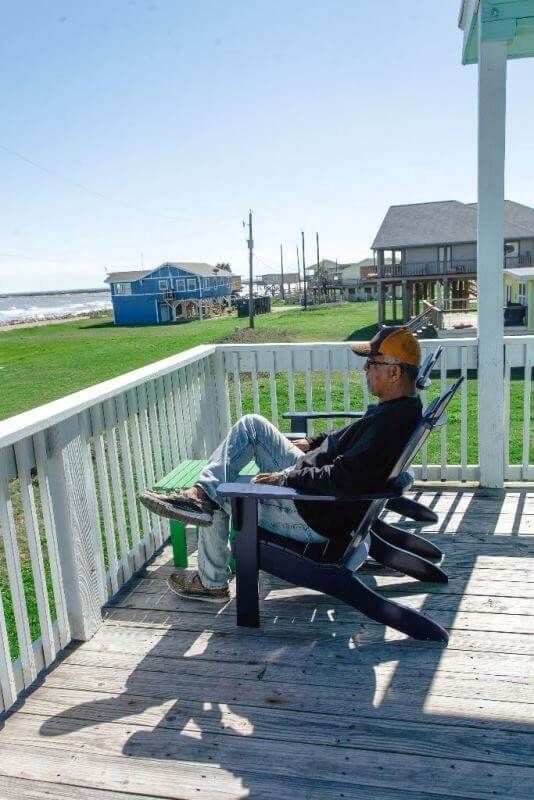 A man is sitting in a chair on a deck overlooking the ocean.
