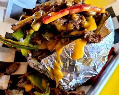 A close up of a potato wrapped in tin foil with cheese and meat