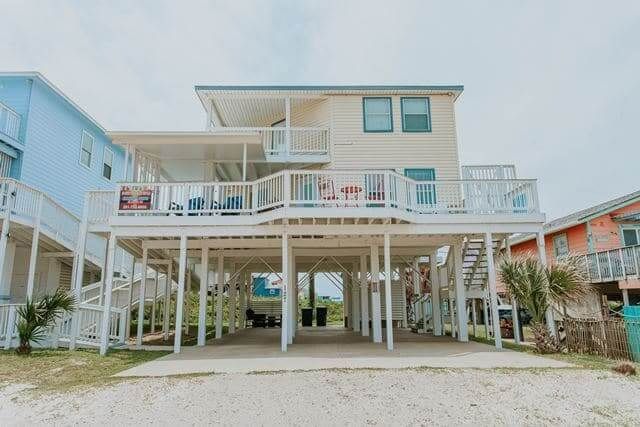 A large white house with a large deck is sitting on top of a sandy beach.