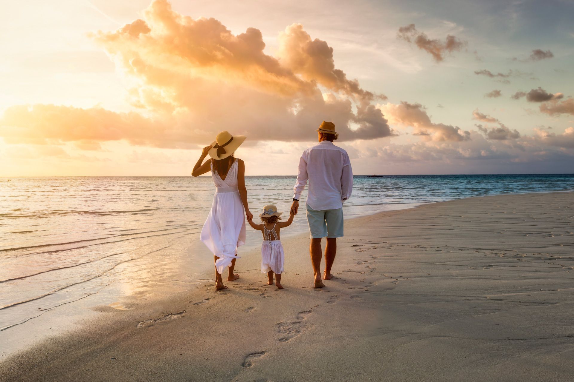 A family is walking on the beach at sunset holding hands.