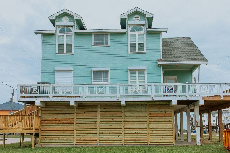 A blue house with a wooden deck and shutters on the windows.