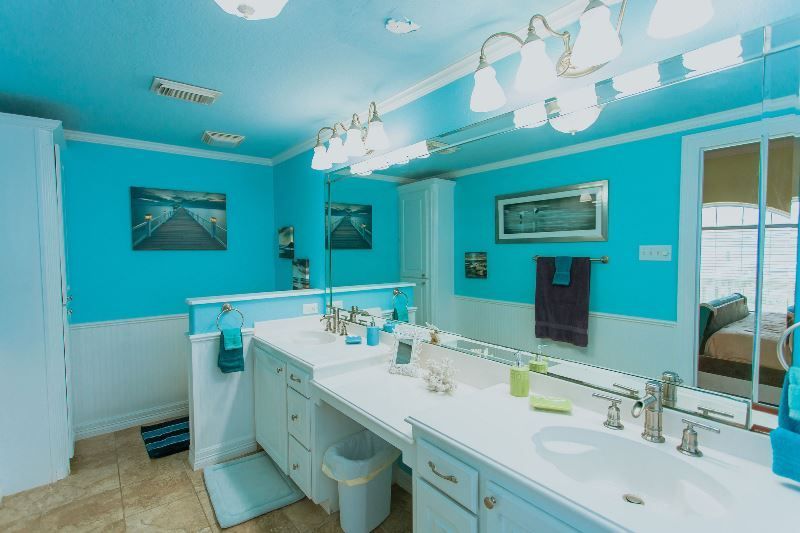 A bathroom with blue walls and white cabinets and two sinks.