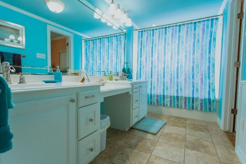 A bathroom with blue walls , white cabinets , a sink , a mirror and a shower curtain.