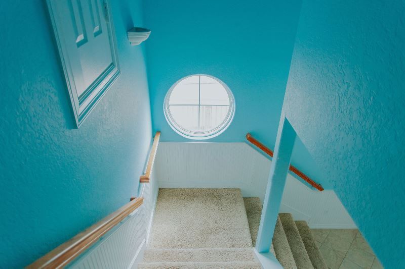 A blue staircase with a round window on the ceiling.