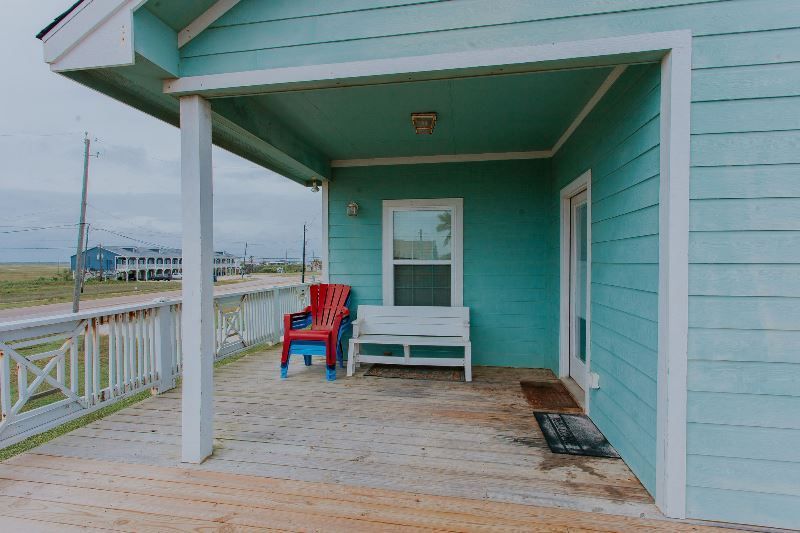 There is a porch with a bench and chairs on it.