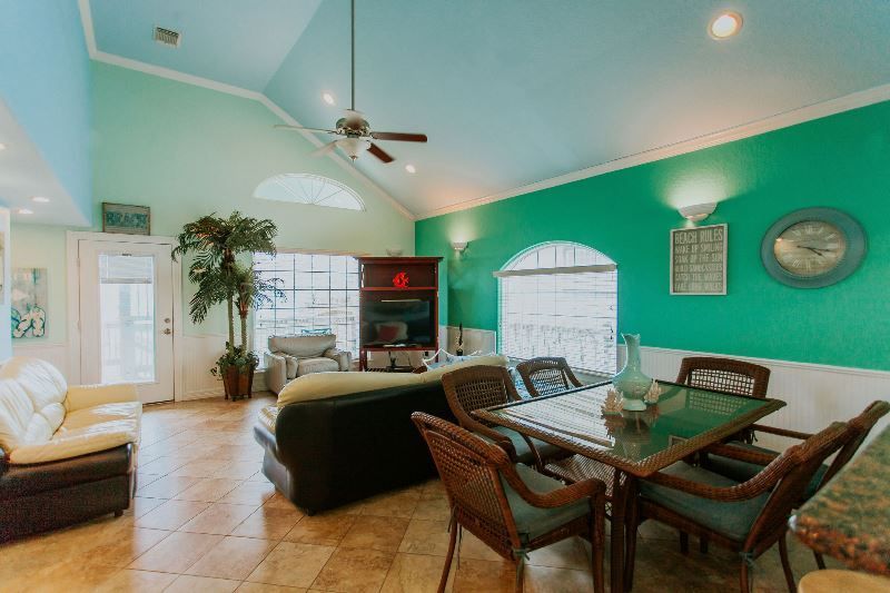 A living room with green walls , a table and chairs , and a ceiling fan.