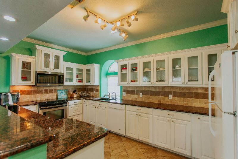A kitchen with white cabinets , granite counter tops , stainless steel appliances and green walls.