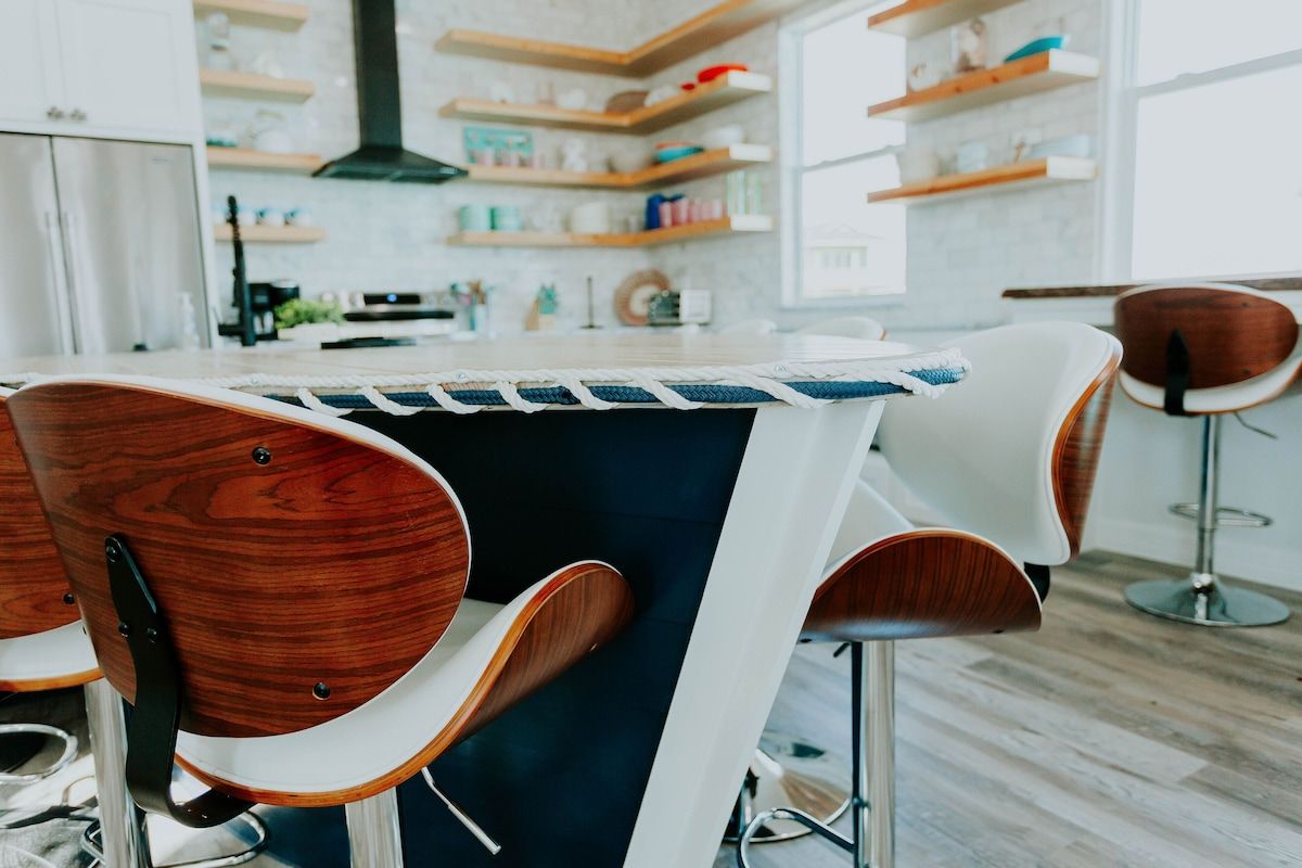 Modern kitchen with a blue island and wooden bar stools, featuring open shelving and a black range hood.